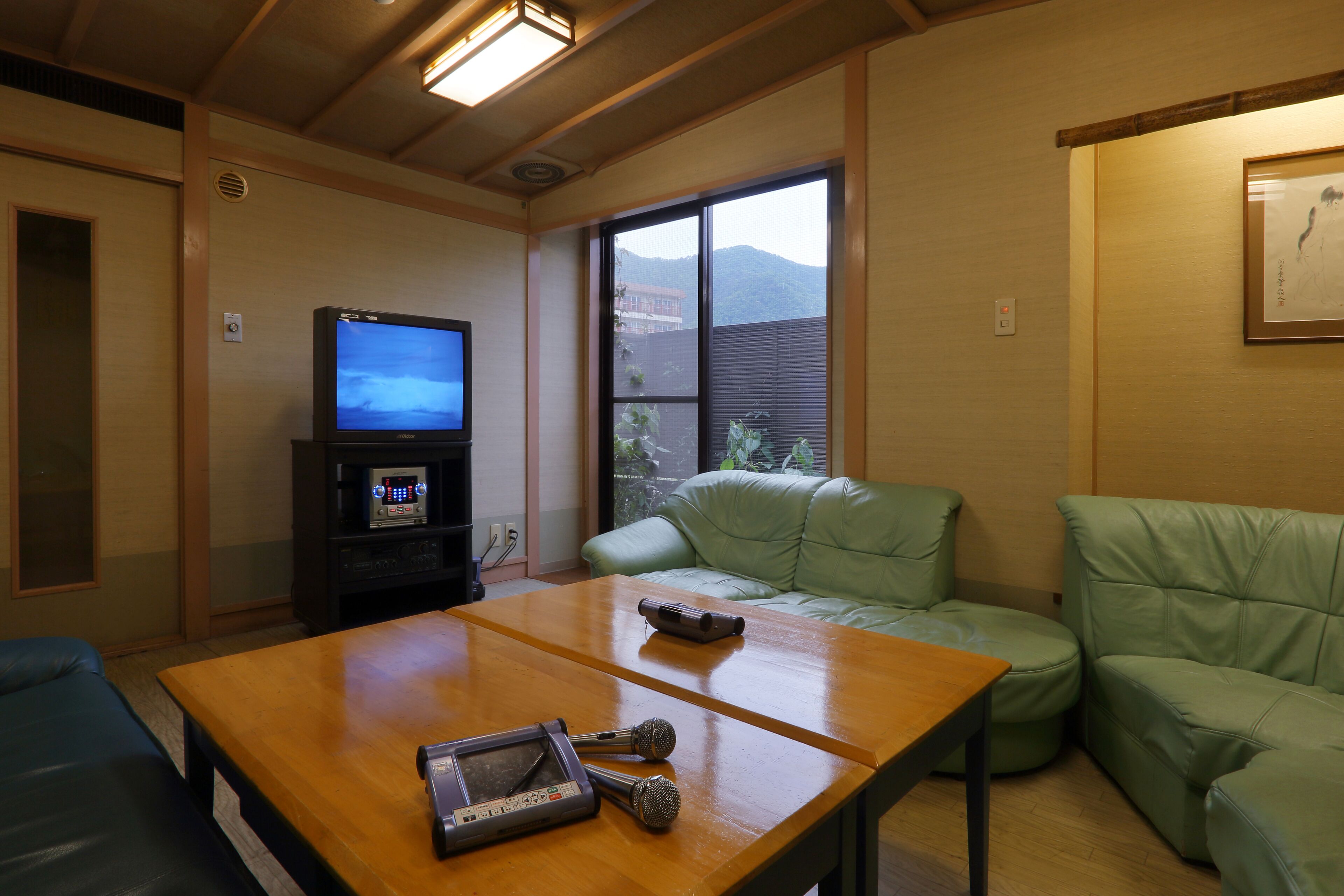 Una habitación con una mesa de madera, un sofá verde, un televisor y una máquina de karaoke.