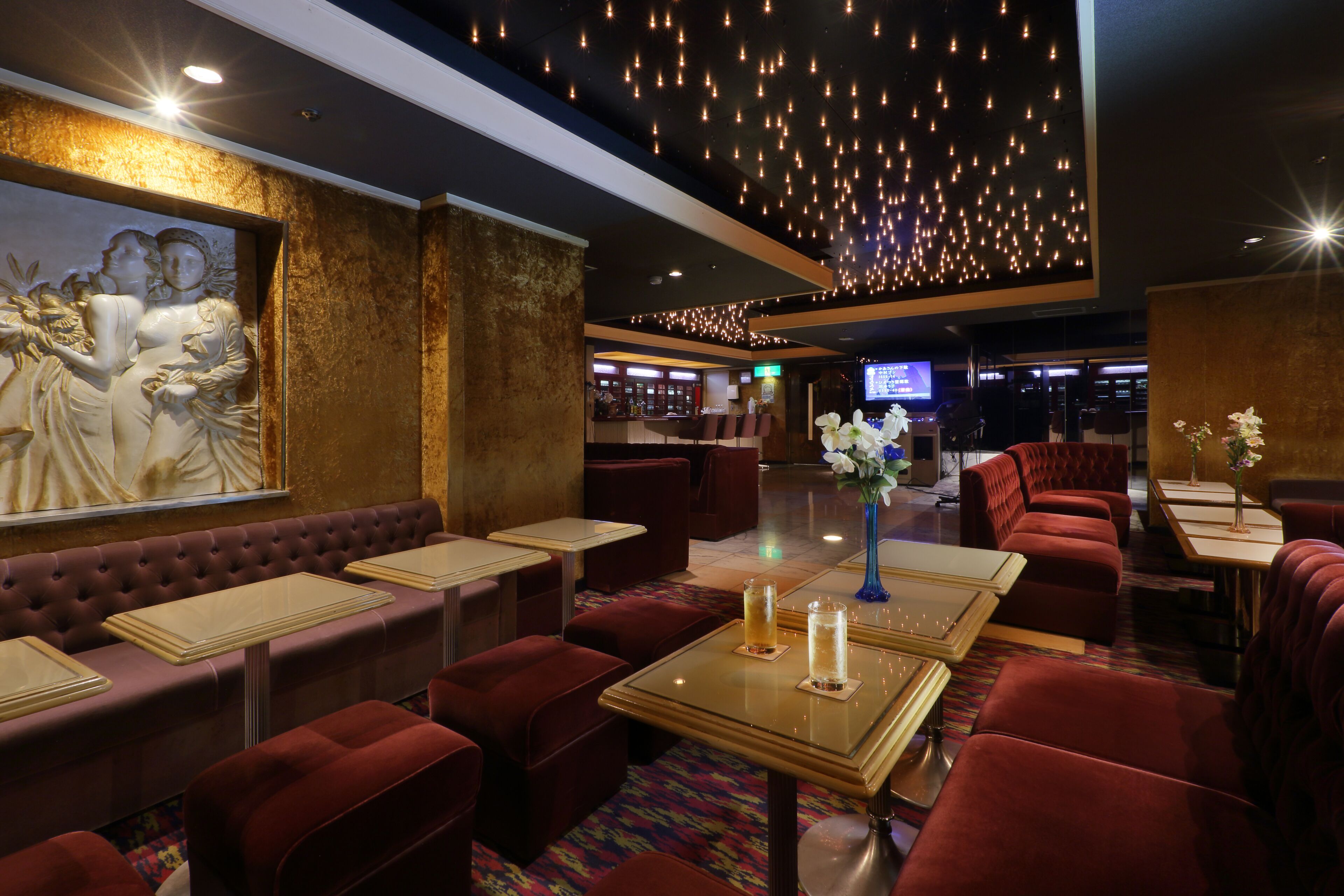 A restaurant with red upholstered booths, a bar in the background, and a ceiling adorned with hanging lights.