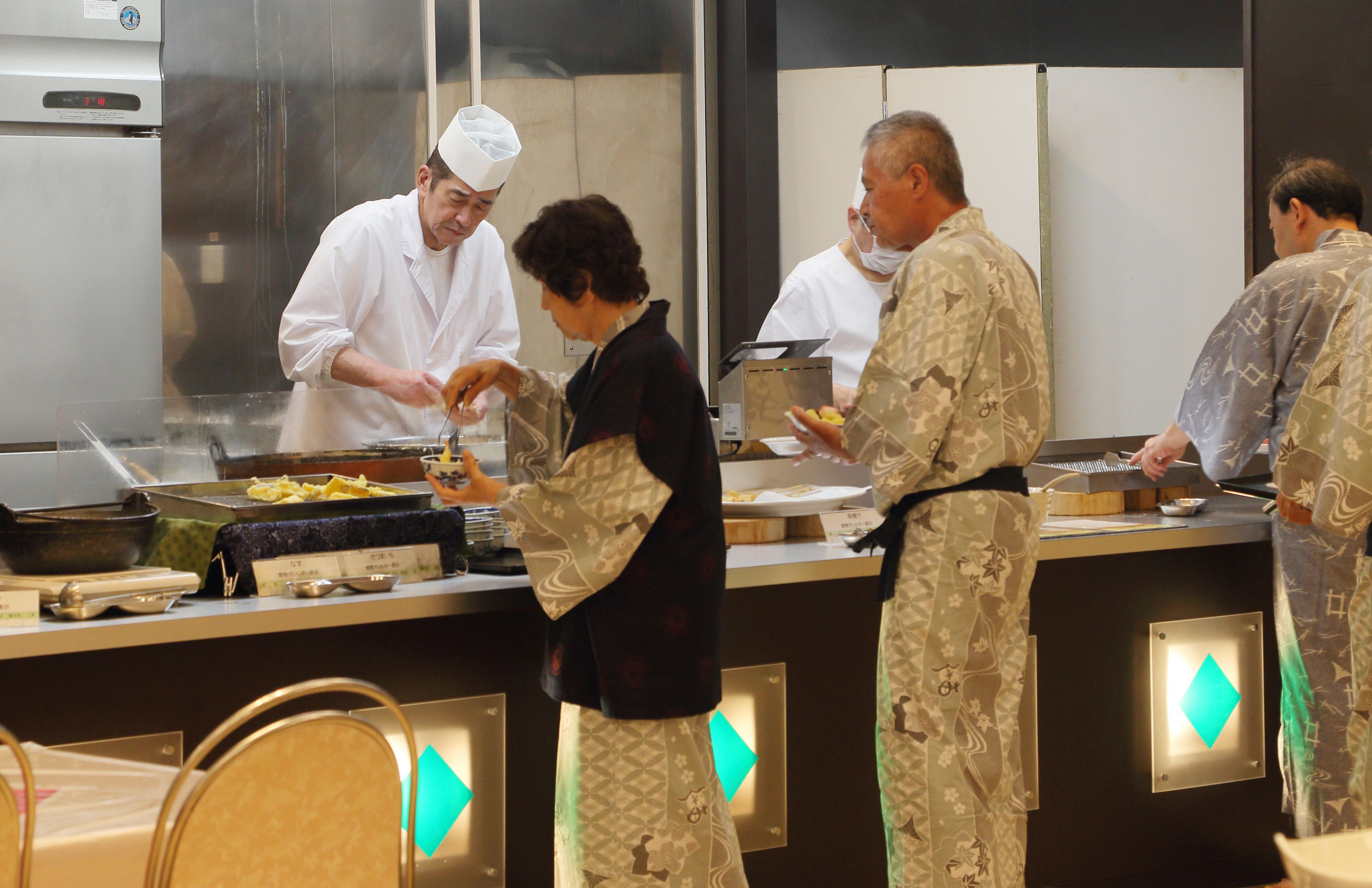 A kitchen area with chefs preparing food, a stainless steel counter, and a refrigerator.