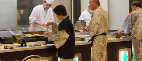 A kitchen area with chefs preparing food, a stainless steel counter, and a refrigerator.