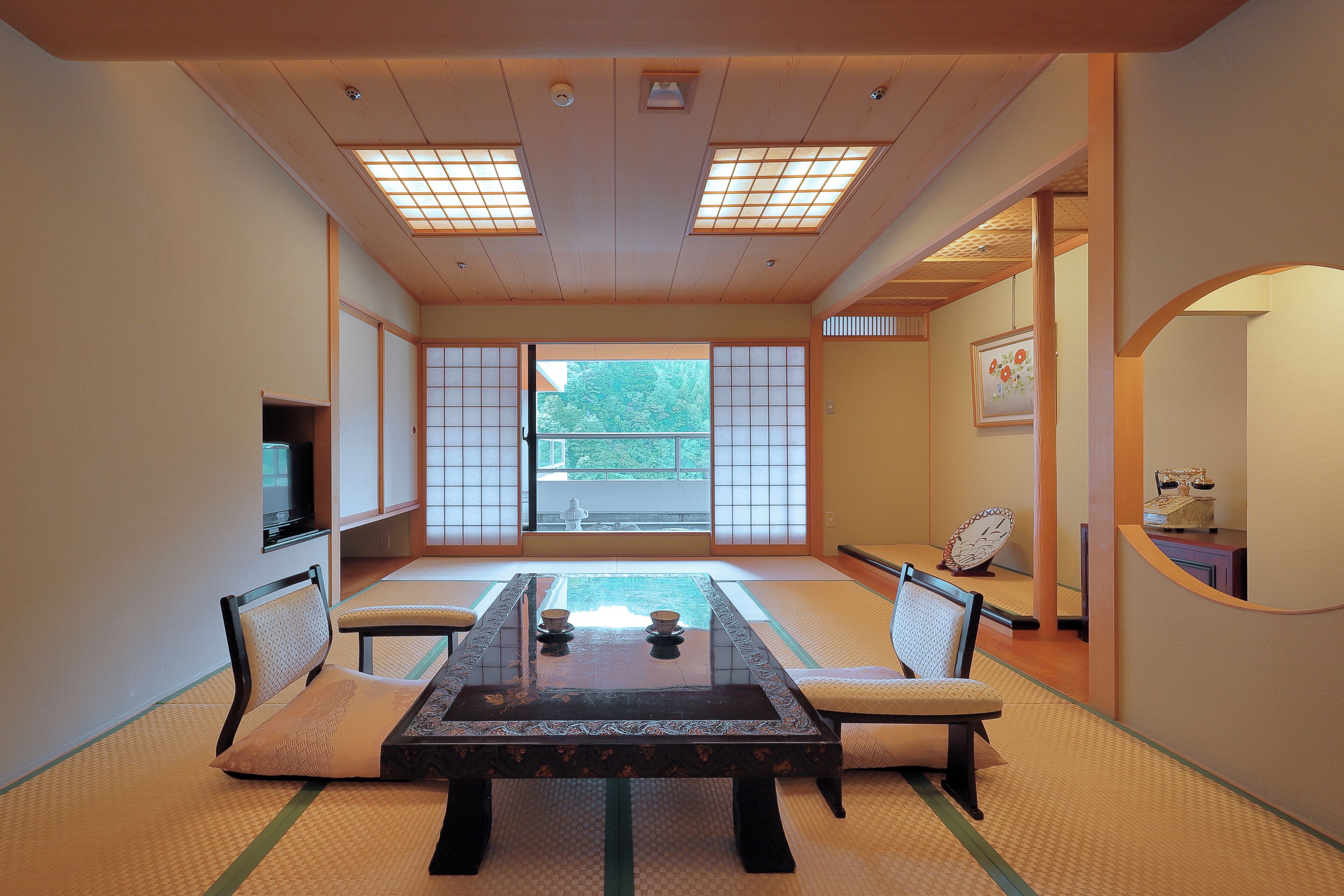 A traditional Japanese room with tatami flooring, a low table with cushions, sliding doors, and a view of greenery outside.