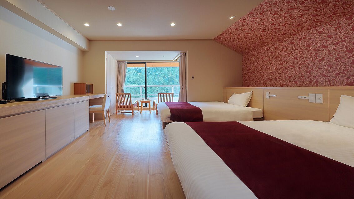 Habitación de hotel con televisor, dos camas, escritorio y balcón con vistas.