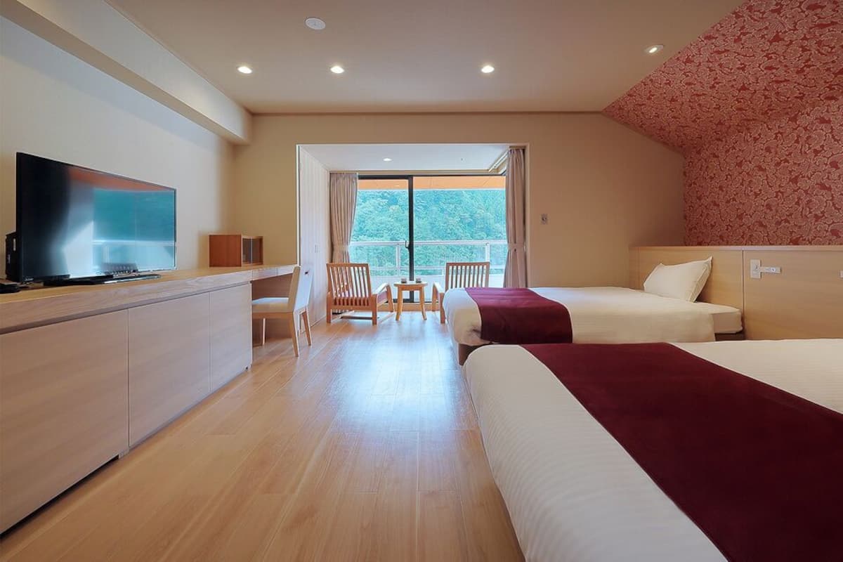 Une chambre d’hôtel équipée d’une télévision, de deux lits, d’un bureau et d’un balcon avec vue.