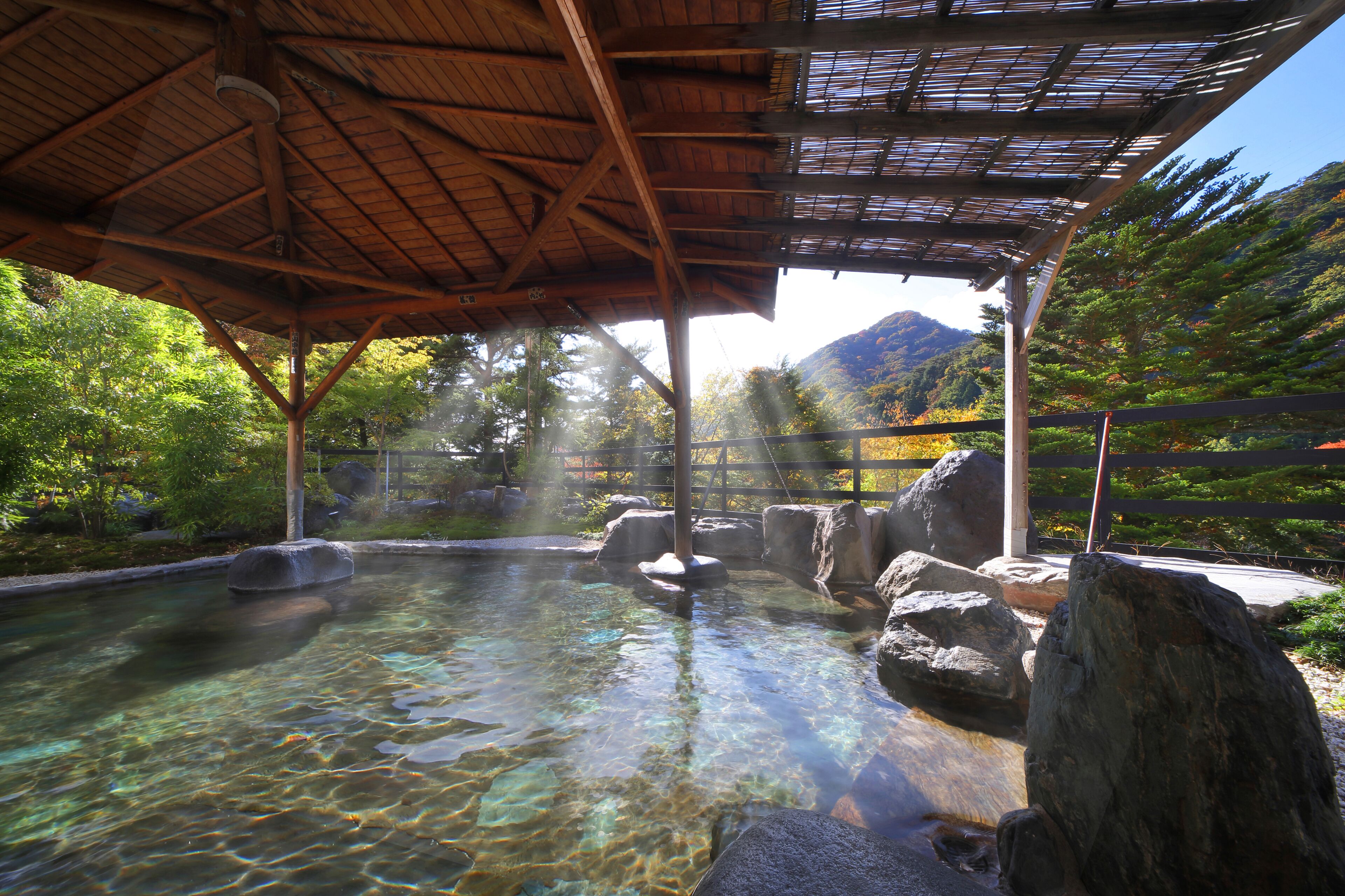 A clear pool with rocks, a wooden pavilion, and a mountainous backdrop.