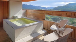 Un balcón con bañera de hidromasaje, terraza de madera y sillas con vistas a un paisaje montañoso.