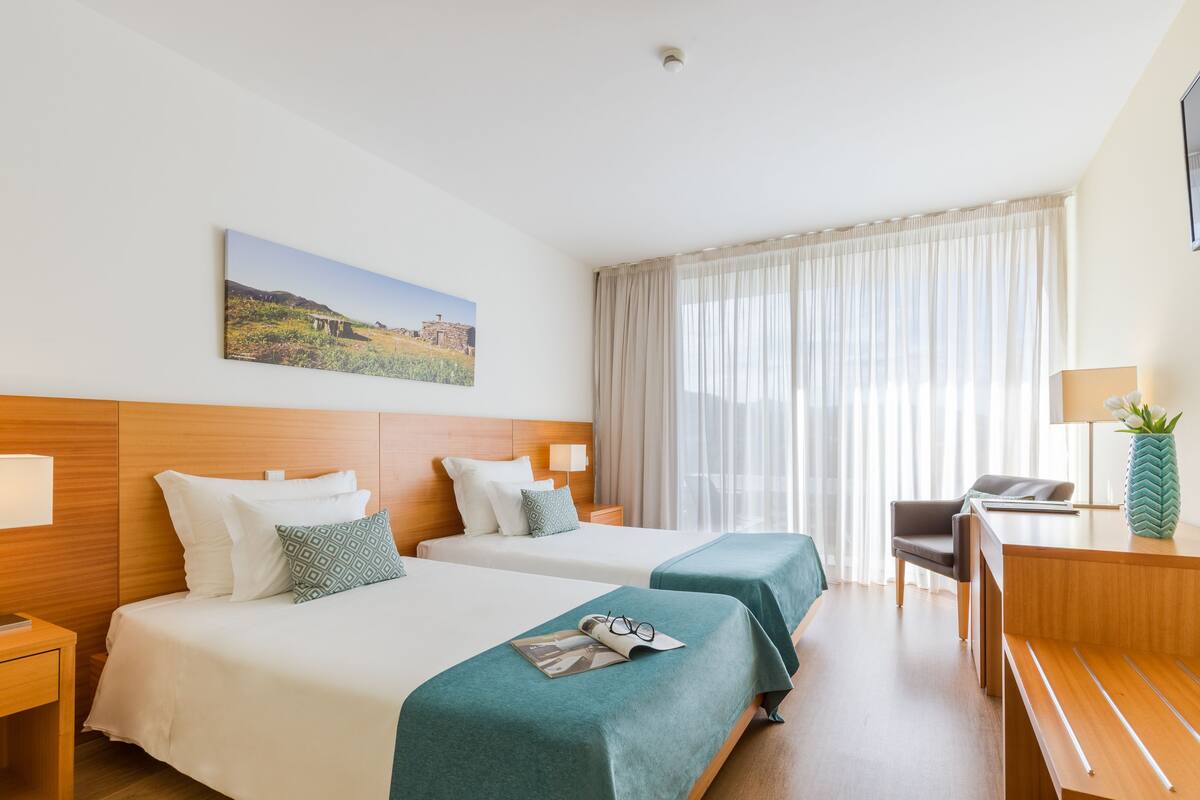 Habitación de hotel con dos camas, un escritorio, una silla, una lámpara y un cuadro en la pared.