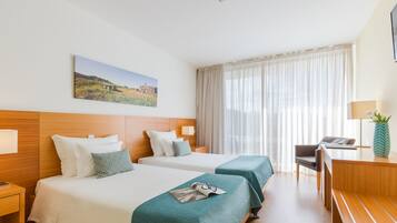 Habitación de hotel con dos camas, un escritorio, una silla, una lámpara y un cuadro en la pared.