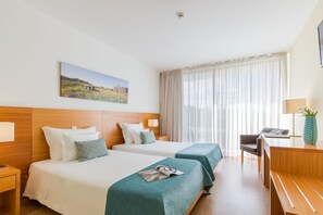 Ein Hotelzimmer mit zwei Betten, einem Schreibtisch, einem Stuhl, einer Lampe und einem Bild an der Wand.