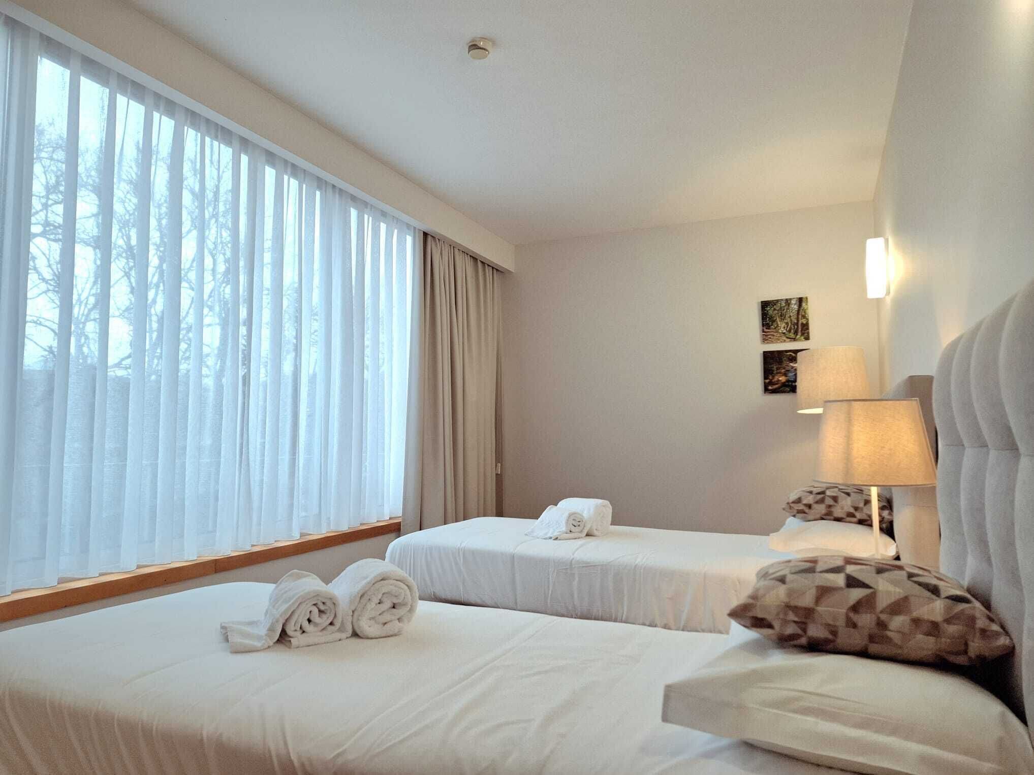 Habitación de hotel con dos camas, una ventana con cortinas, una lámpara y una obra de arte en la pared.
