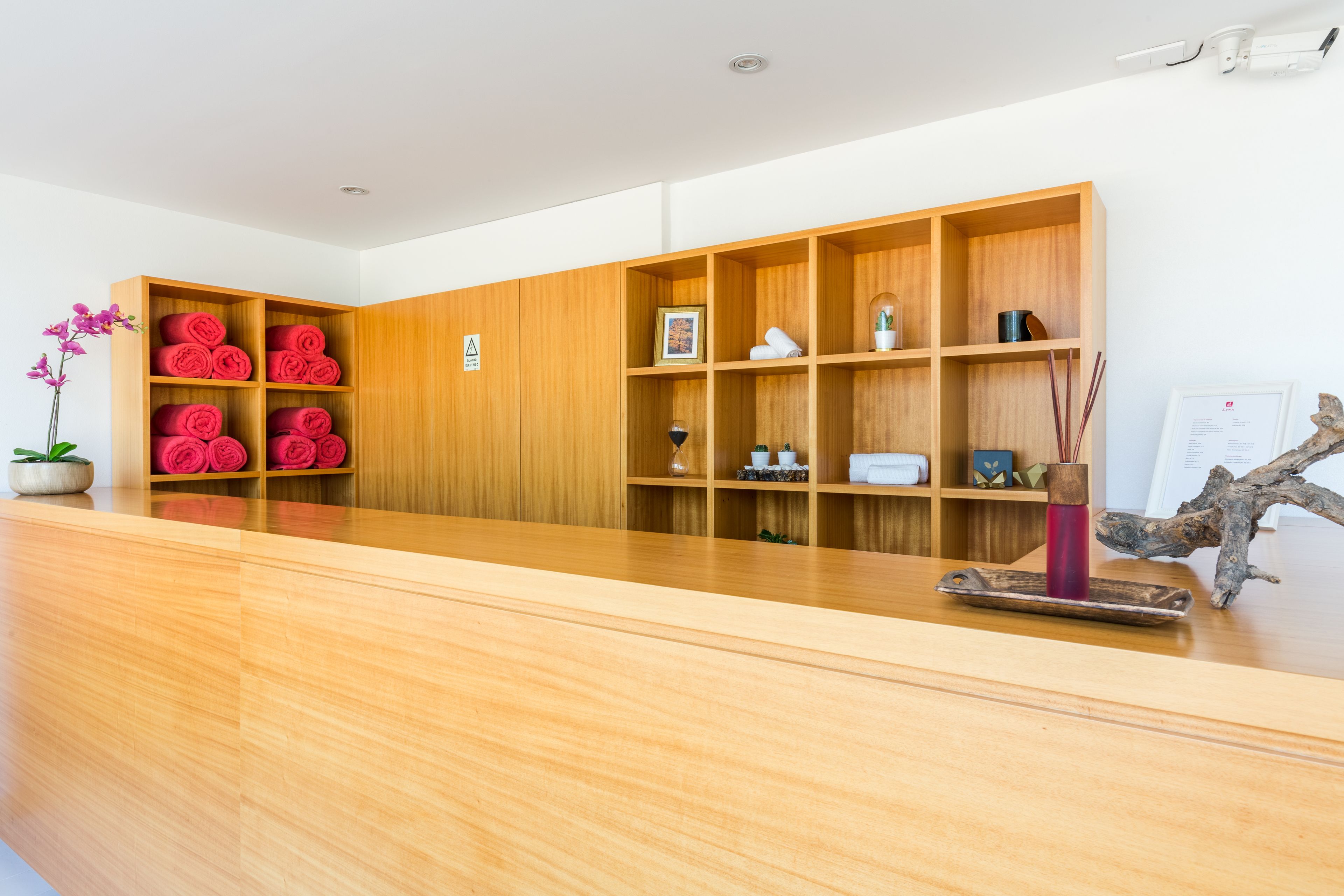 Een receptiegedeelte met een houten receptiebalie, een potorkidee en een houten plank met opgerolde handdoeken en decoratieve voorwerpen.