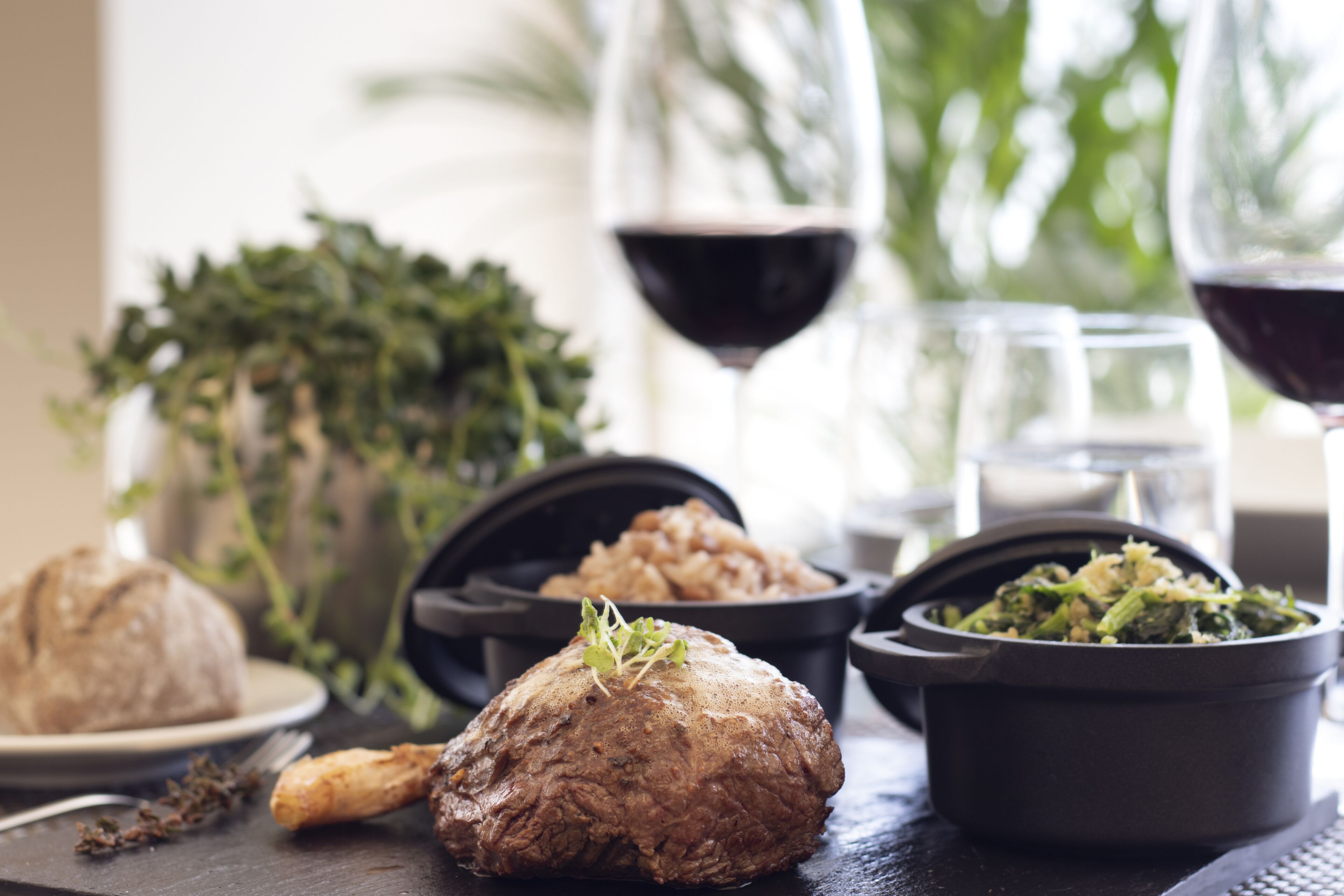 A dining table with various dishes, including a large meatball, a bowl of greens, and a glass of red wine.