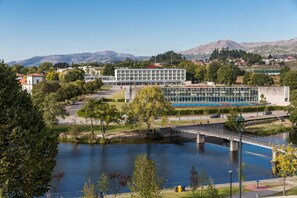 Un edificio moderno con fachada de vidrio, un puente sobre un río y montañas al fondo.