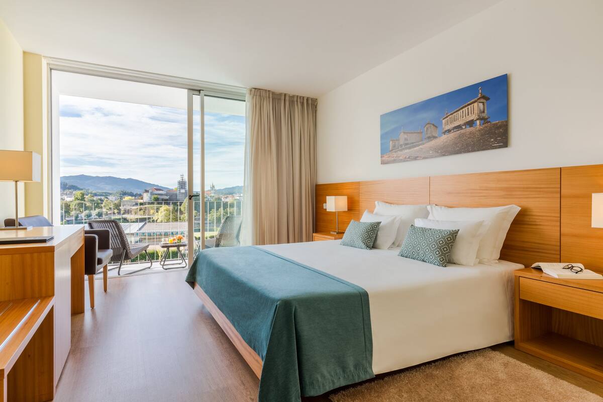 Habitación de hotel con una cama grande, un escritorio, una silla, vistas de la ciudad y un cuadro en la pared.