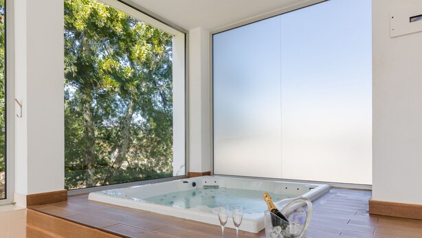 A spa area with a hot tub, wooden seating, and a view of trees through a large window.