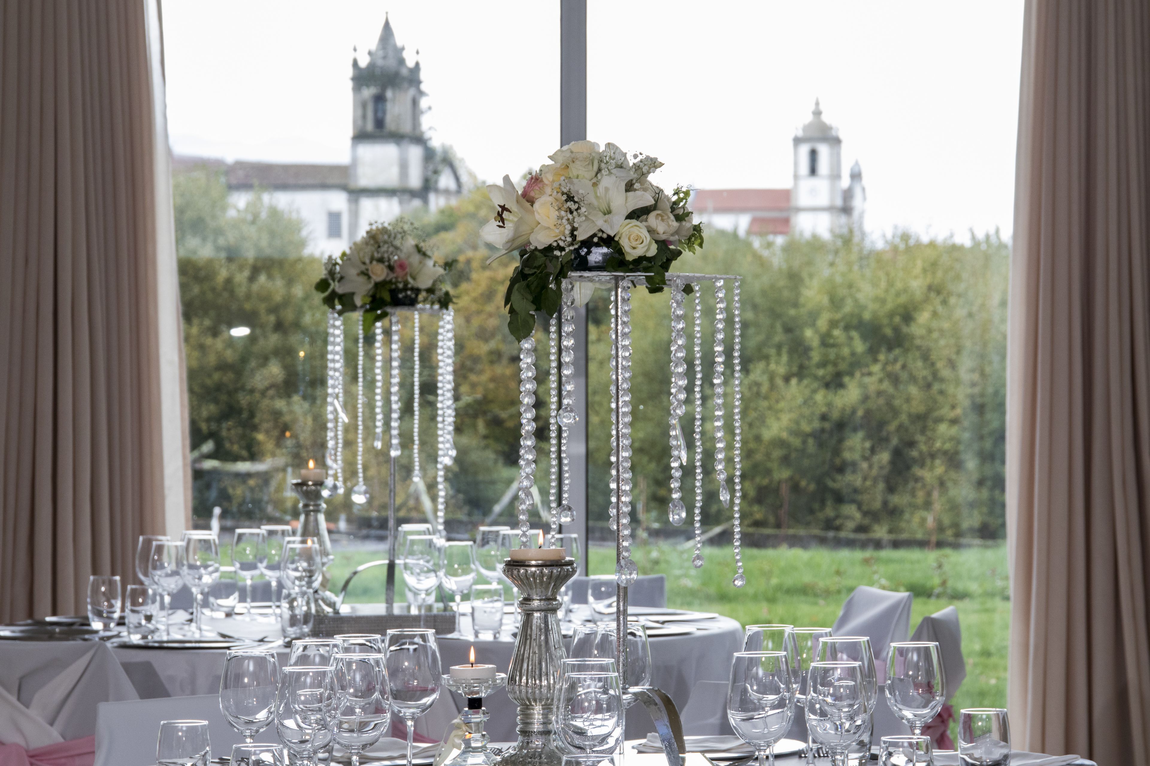 Una mesa dispuesta para un evento formal, con adornos de cristal, un centro de mesa con velas y una vista de un edificio histórico al fondo.