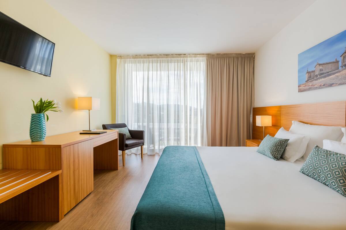 Habitación de hotel con cama, escritorio, silla, televisor y un cuadro en la pared.