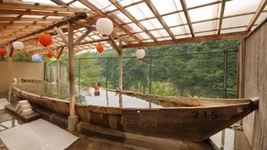 A traditional wooden boat-shaped hot spring bath with a number '215' on the side, surrounded by a wooden structure with a glass roof and red lanterns. - Kinugawa Niouson Plaza (Nikko)