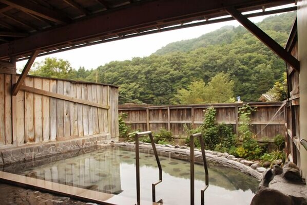 A traditional wooden bathhouse with a stone floor and a wooden fence.