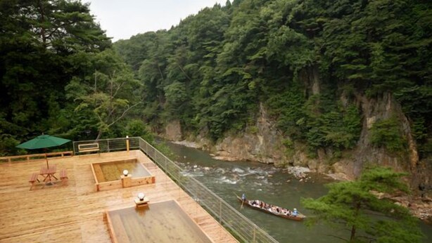 A wooden deck overlooking a river with a canoe, surrounded by dense forest. - Kinugawa Niouson Plaza (Nikko)