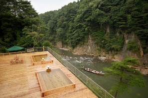 A wooden deck overlooking a river with a canoe, surrounded by dense forest.