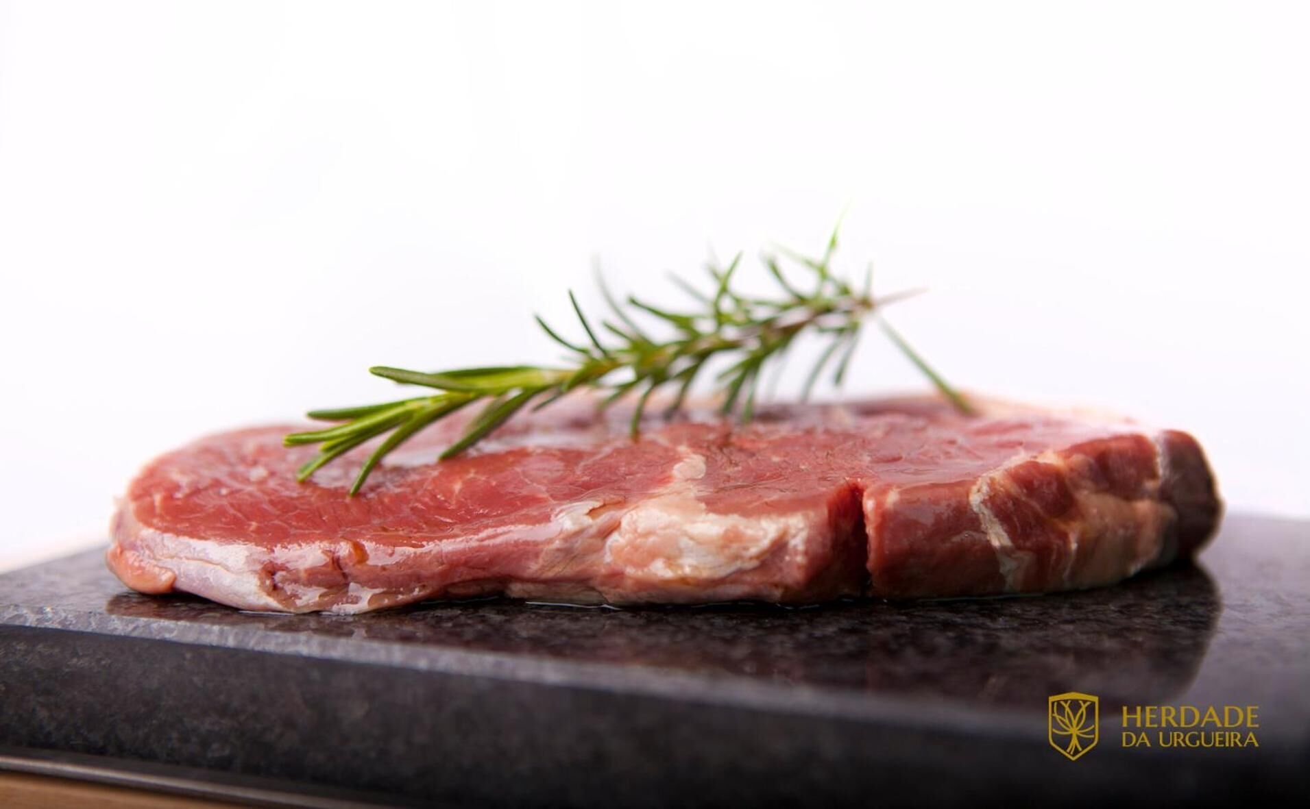 Un steak cru, garni de romarin, sur une planche à découper sombre.