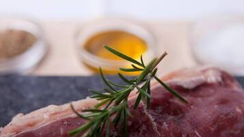 Primer plano de carne cruda con romero y dos recipientes pequeños de condimentos y aceite.