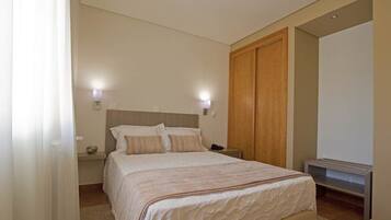 Een slaapkamer met een groot bed, nachtlampjes, een houten garderobe en een tv-meubel.