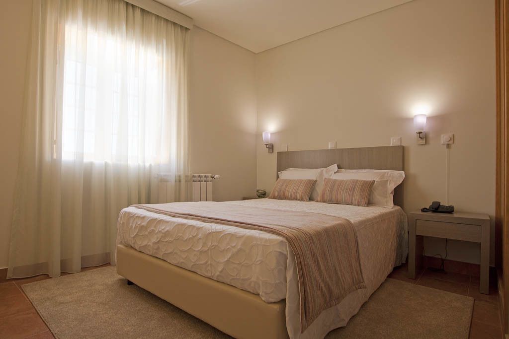 Un dormitorio con una cama grande, mesitas de noche y un ventanal con cortinas.