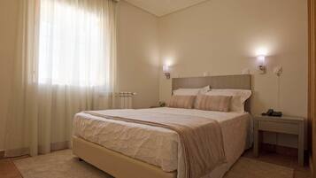 Un dormitorio con una cama grande, mesitas de noche y un ventanal con cortinas.