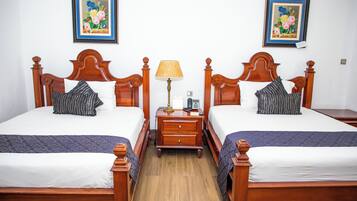 Habitación de hotel con dos camas de madera, una mesita de noche con lámpara y dos cuadros enmarcados con motivos florales en la pared.