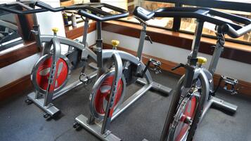 Three stationary bikes in a room with a window and a wooden floor.
