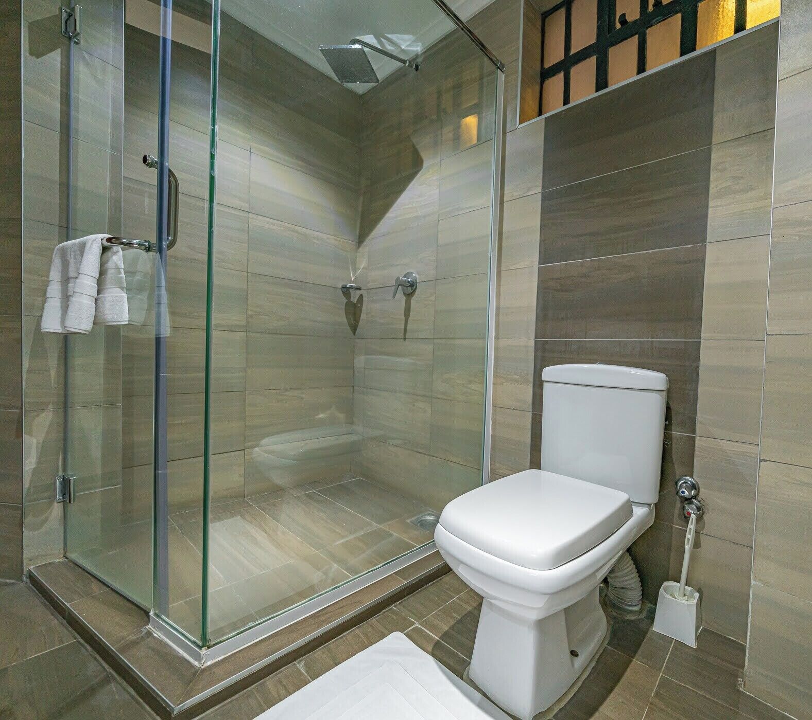 Un baño moderno con ducha envuelta en vidrio, inodoro blanco y toallero con toallas.