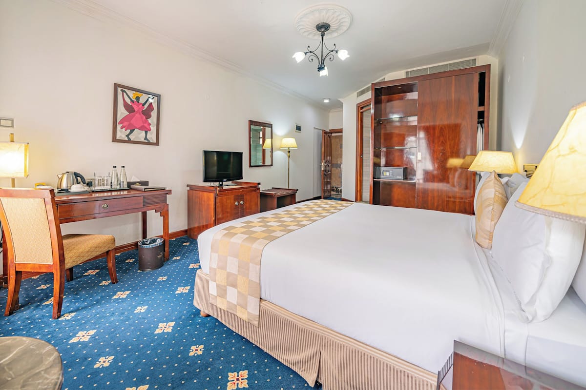 Una habitación de hotel con cama, escritorio, silla, televisor y armario.