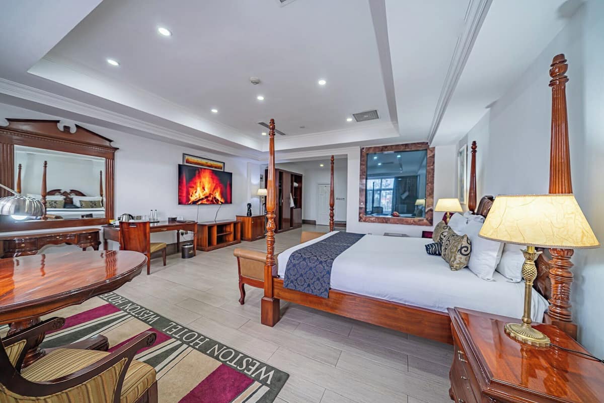 Habitación de hotel con cama con dosel, escritorio con silla, televisor y chimenea.