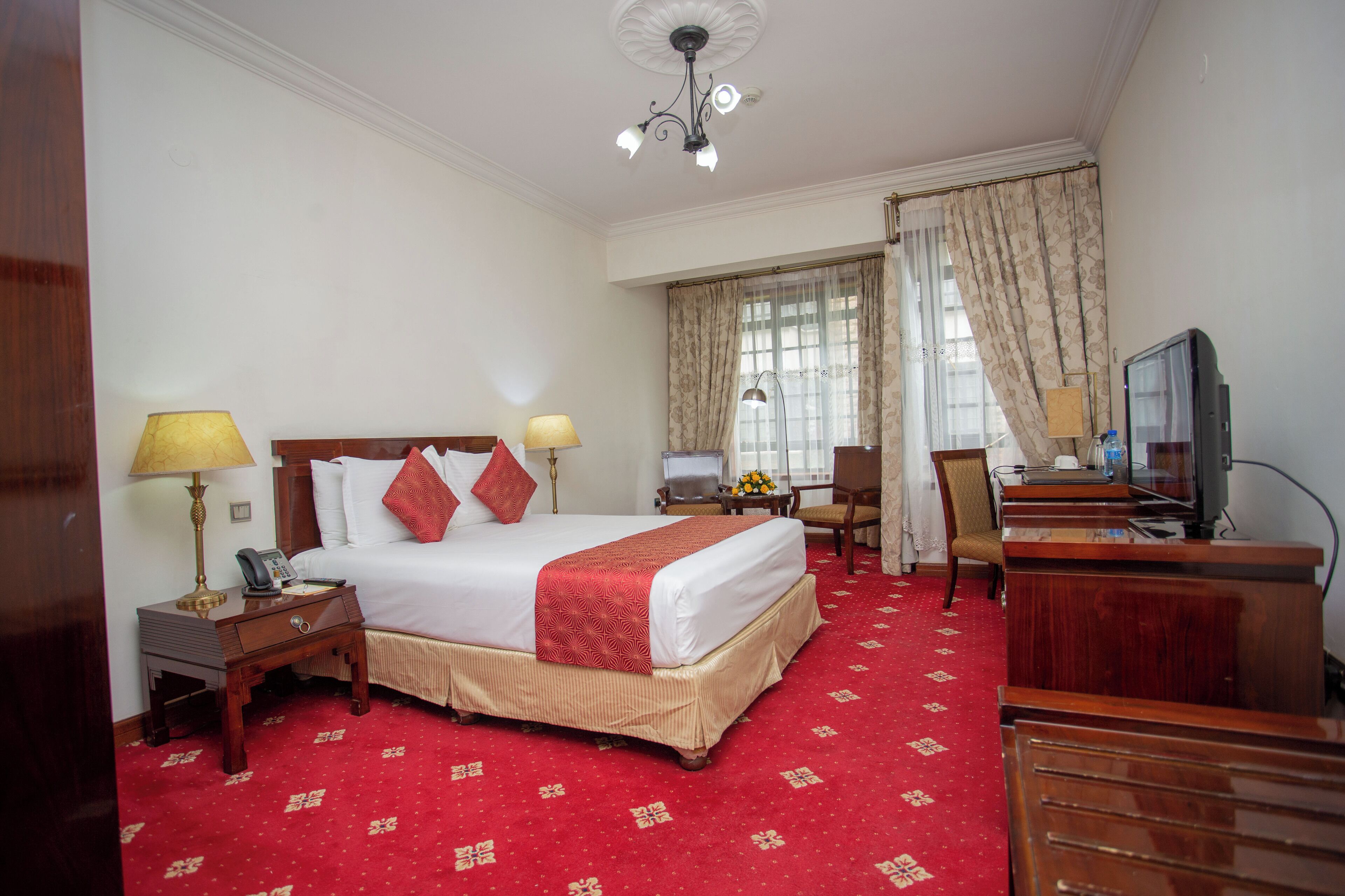 Quarto de hotel com uma cama grande, uma escrivaninha com computador, uma cadeira e uma televisão.