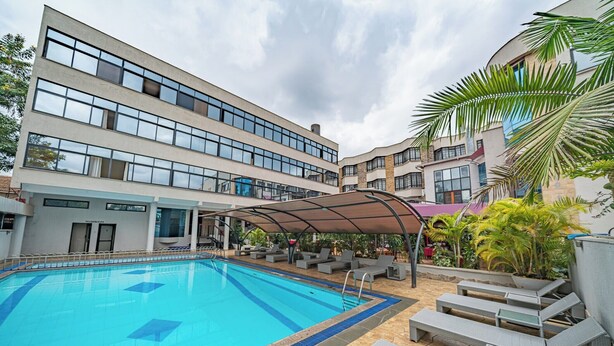 A swimming pool with lounge chairs and a covered seating area, surrounded by buildings with large windows and a palm tree. - Weston Hotel (Nairobi)