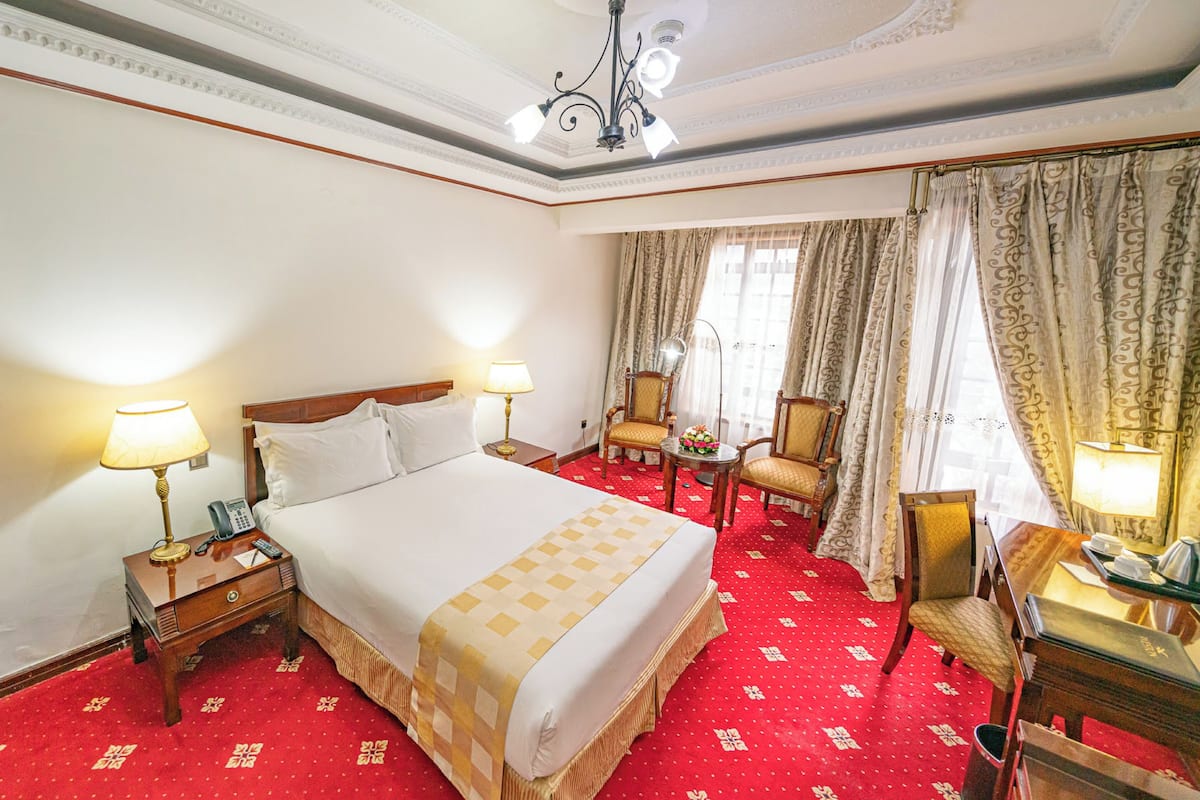Una habitación de hotel con una cama grande, dos mesitas de noche, un escritorio con silla, una pequeña mesa con una silla y un candelabro.