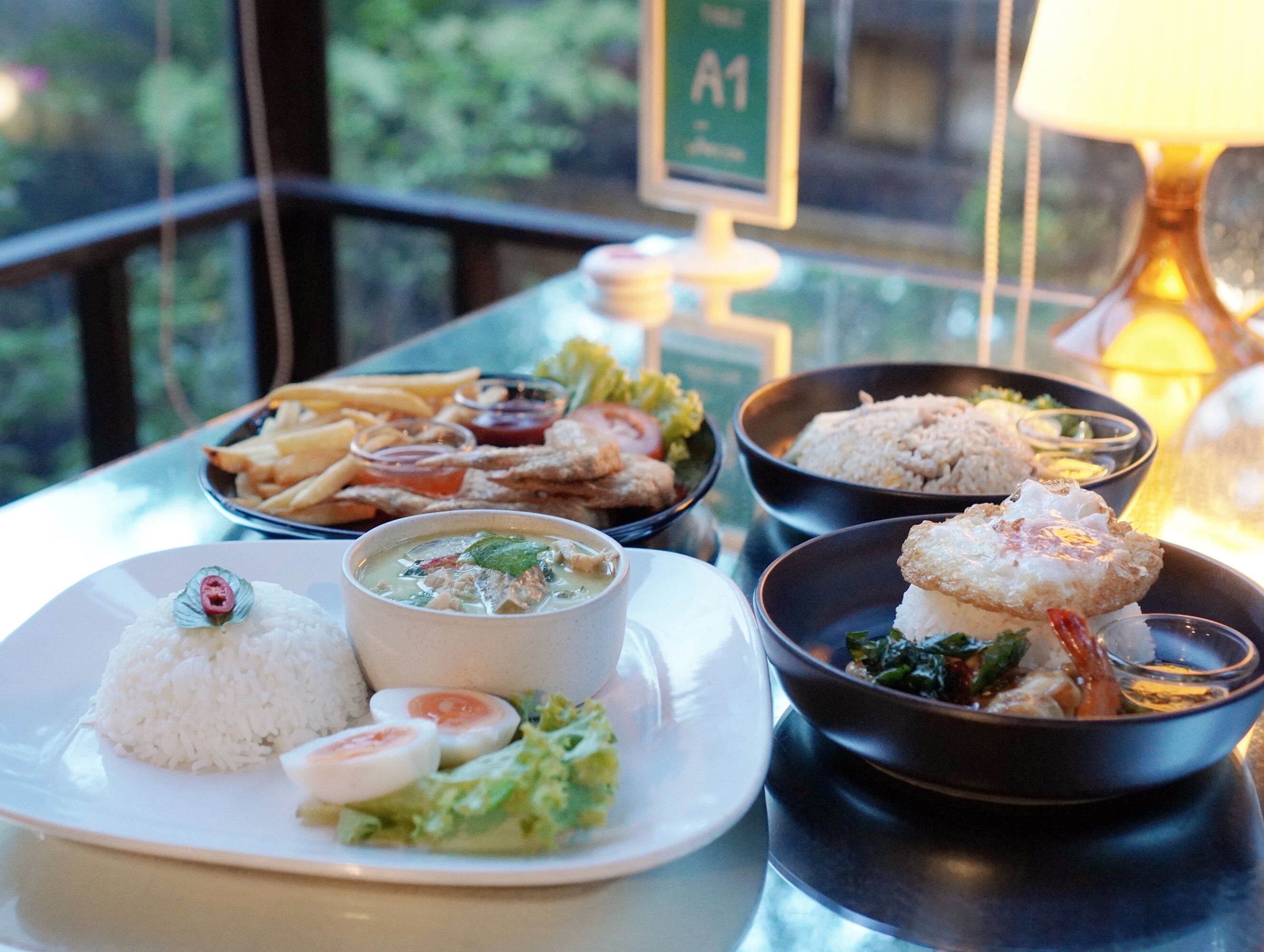 Una mesa con diferentes platos, incluyendo arroz, sopa y comida frita, con vistas a la vegetación.