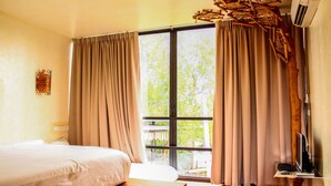 A bedroom with a large window, a bed, a wooden bedside table, and a woven stool. - Bangkok Tree House (Phra Pradaeng)