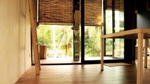 A room with a wooden floor, a table, and a view of greenery through a glass door. - Bangkok Tree House (Phra Pradaeng)