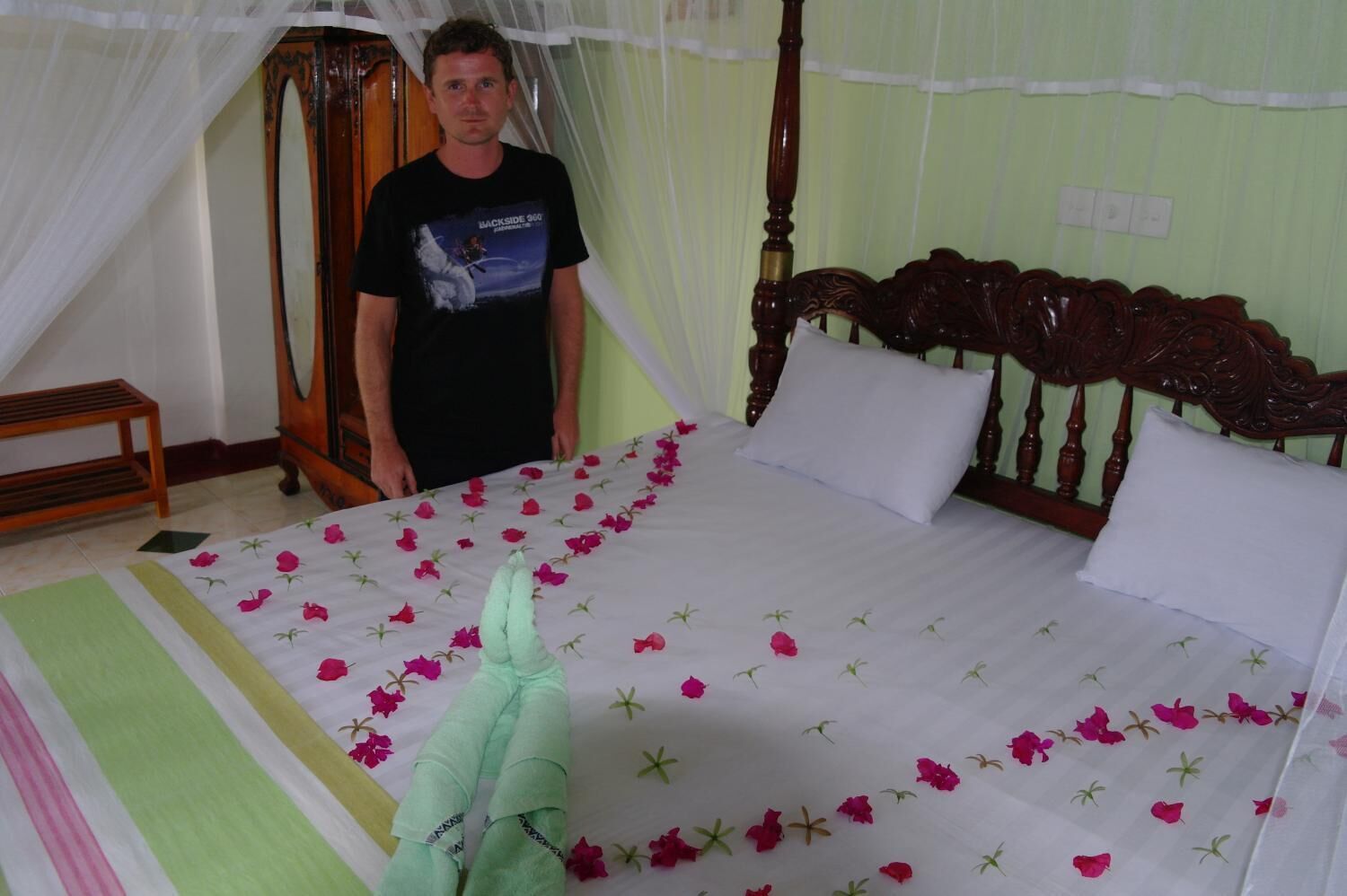 A bed with a floral bedspread, a wooden headboard, and a person standing beside it.