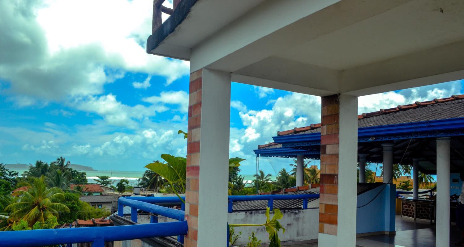 A covered outdoor area with a view of the ocean, featuring blue railings and a tiled roof.