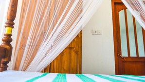 Una cama con colcha a rayas, cabecera de madera y mosquitero blanco.