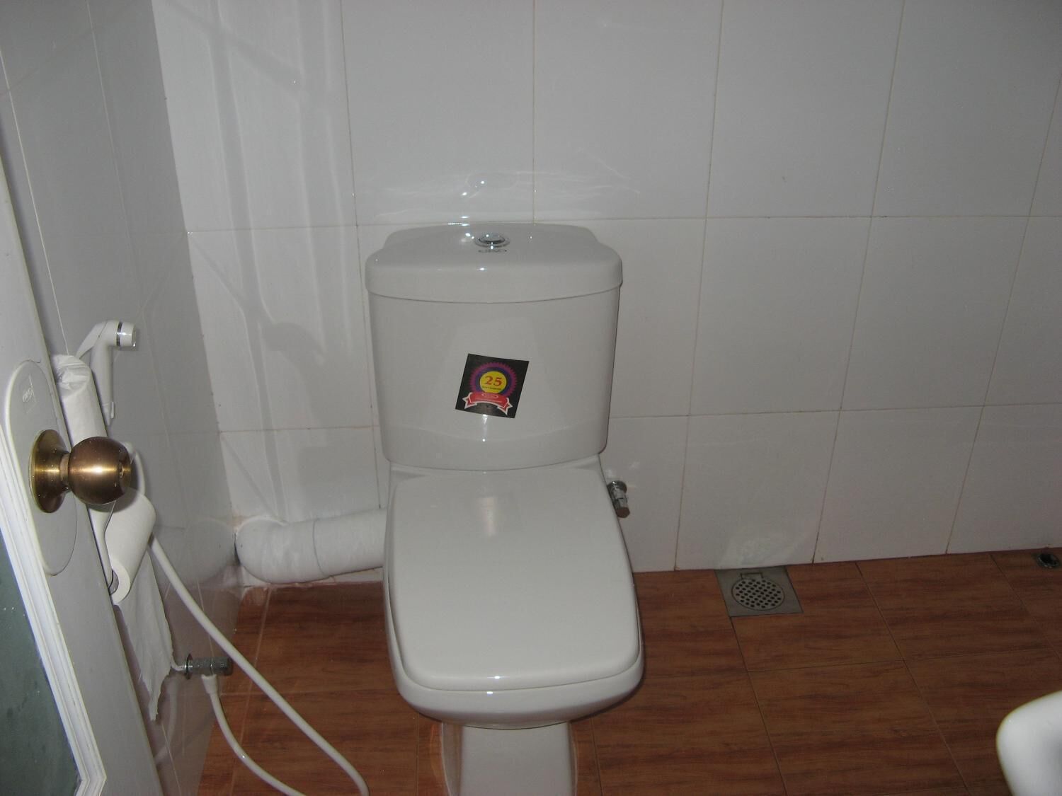 A toilet with a sticker on the tank, a white door with a brass handle, and a wooden floor.