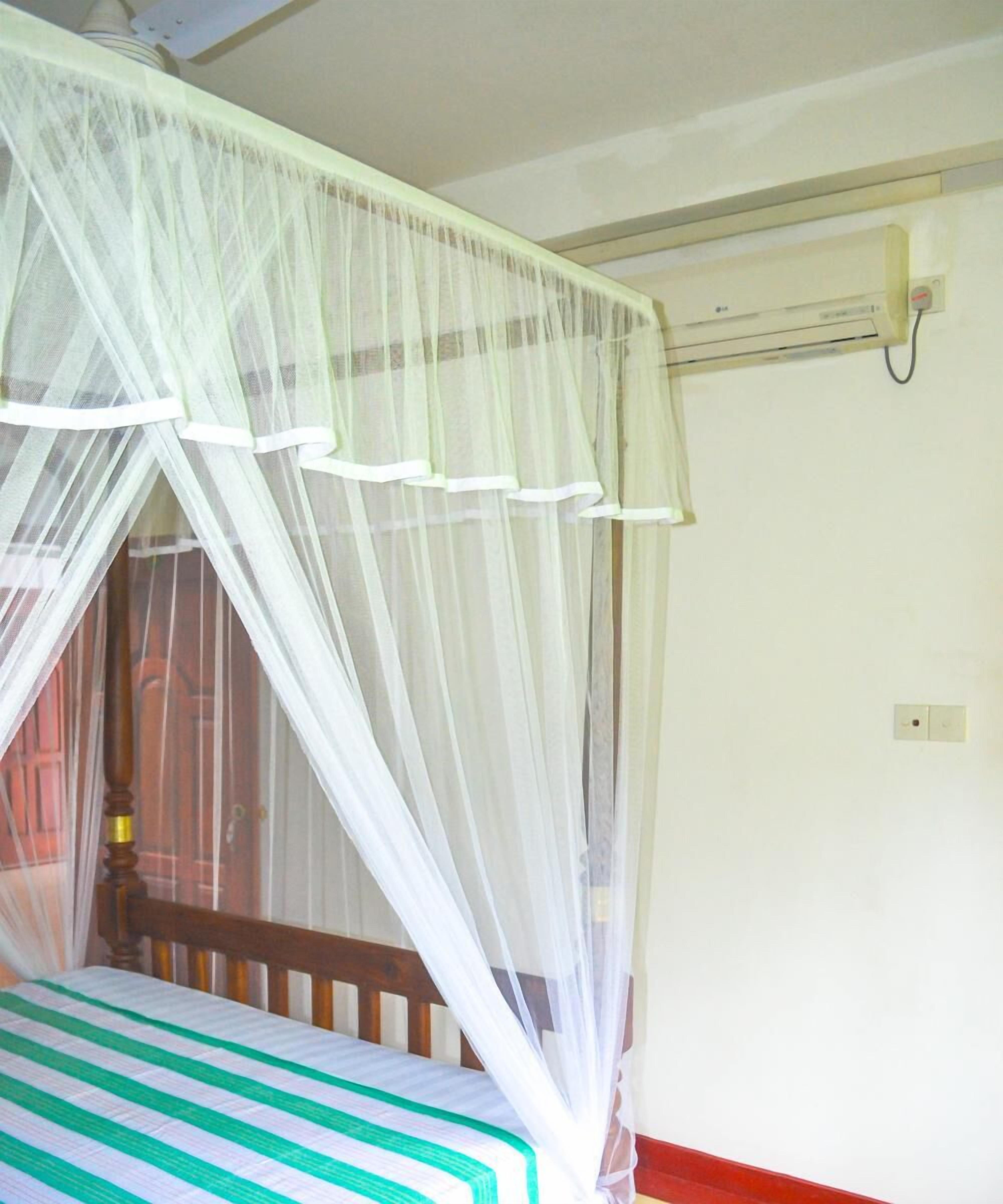 A bed with a striped bedspread, a mosquito net, and a wooden headboard.