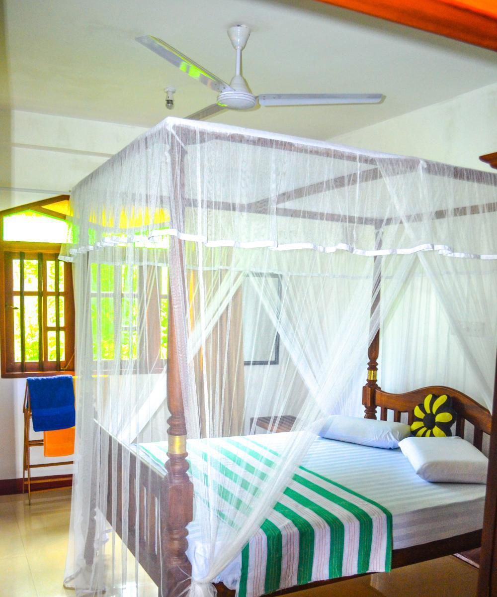 A four-poster bed with a canopy, a ceiling fan, and a window with curtains.