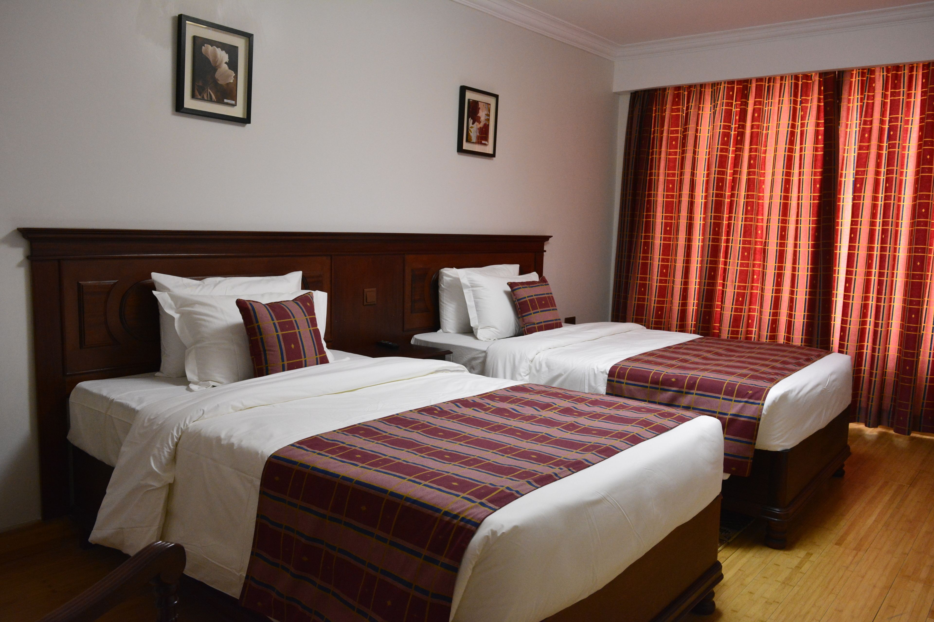 Una habitación de hotel con dos camas individuales, cabeceros de madera, ropa de cama blanca y cortinas rojas.