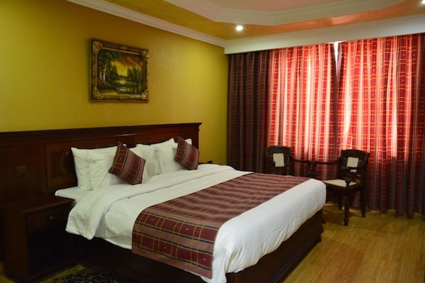 Una habitación de hotel con una cama grande, una mesita de noche, una silla y un cuadro en la pared.