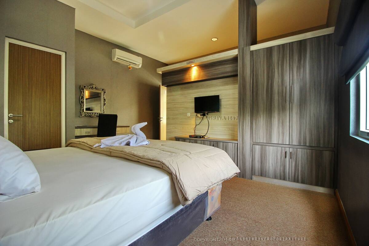 A hotel room with a bed, a TV, and a mirror on the wall.
