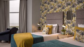 Habitación de hotel con dos camas, vistas al mar y papel tapiz floral.